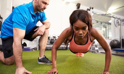 Young,Woman,Doing,Push,Ups,Under,Supervision,Of,A,Trainer